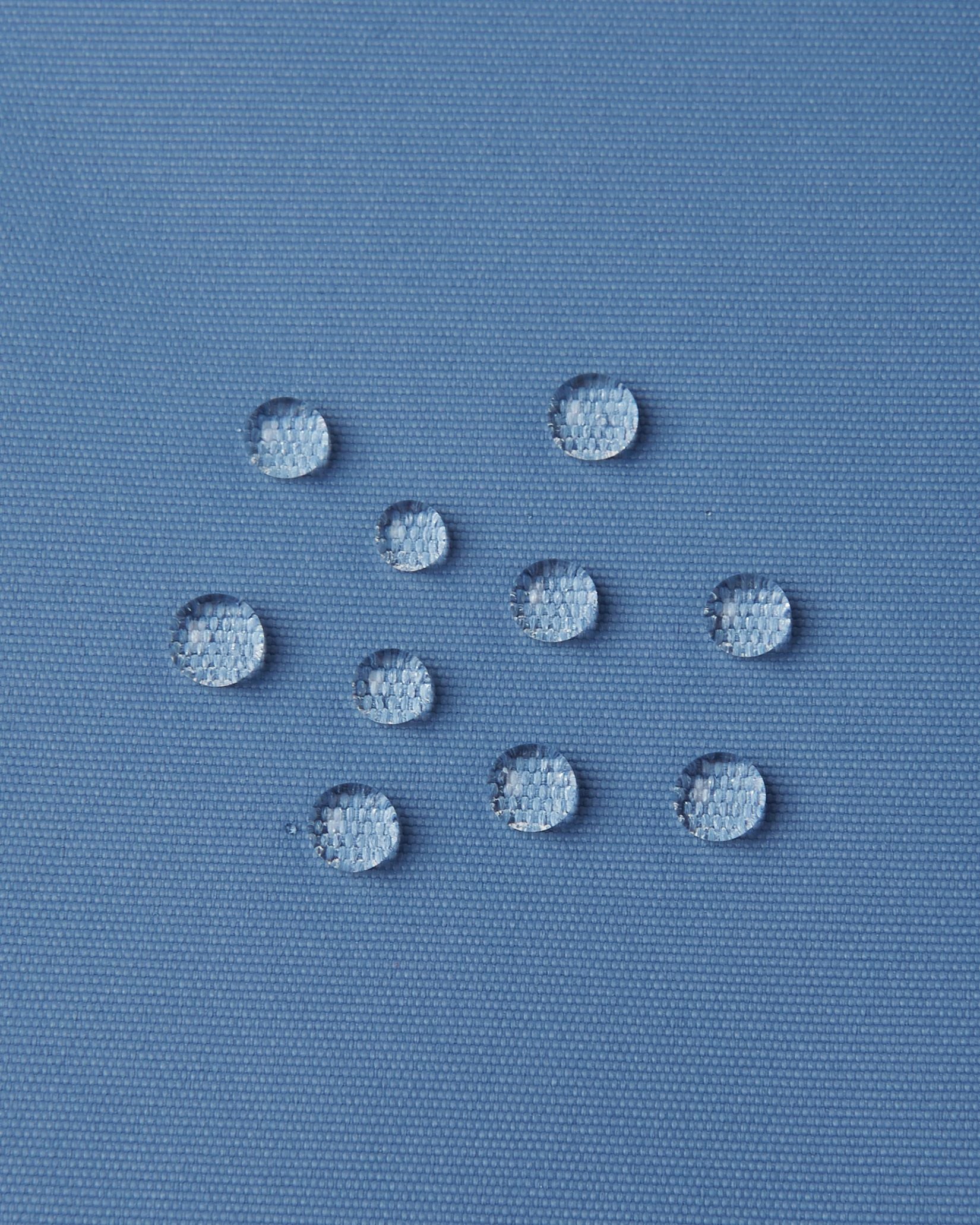 Macro close-up of water droplets actively beading and rolling off the blue ocean outer shell of the Reima Wingon kids' ski pants, visually highlighting the high-performance breathable and waterproof Reimatec technology.