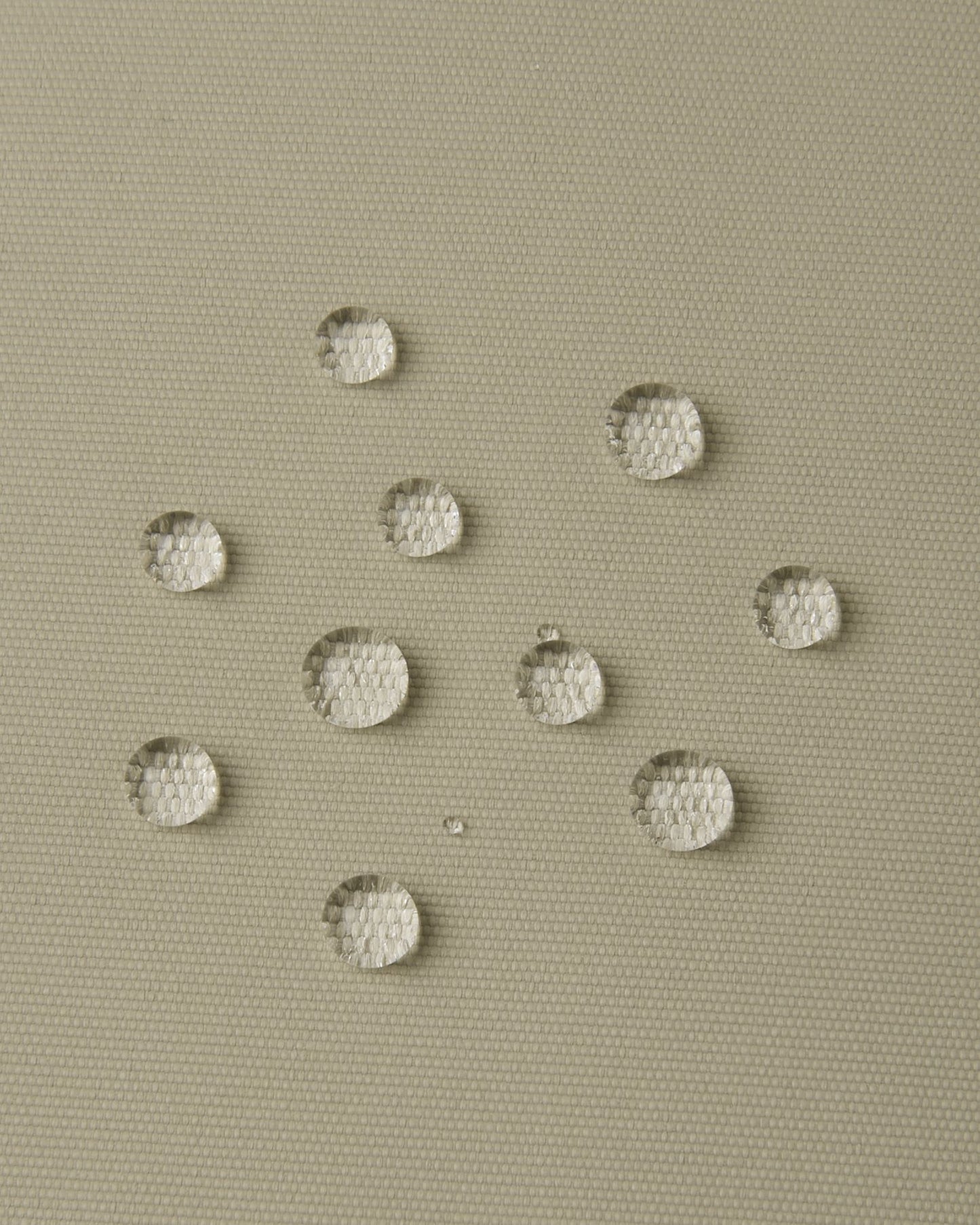 Macro close-up of water droplets actively beading and rolling off the earthy beige outer shell of the Reima Wingon kids' ski pants, visually highlighting the high-performance breathable and waterproof Reimatec technology.