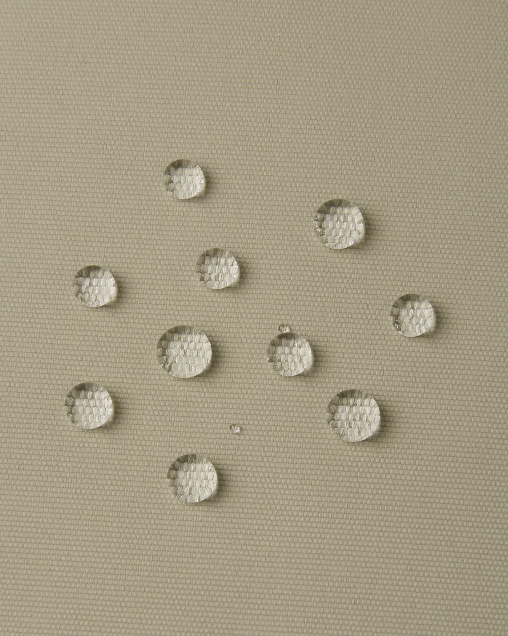 Macro close-up of water droplets actively beading and rolling off the earthy beige outer shell of the Reima Wingon kids' ski pants, visually highlighting the high-performance breathable and waterproof Reimatec technology.