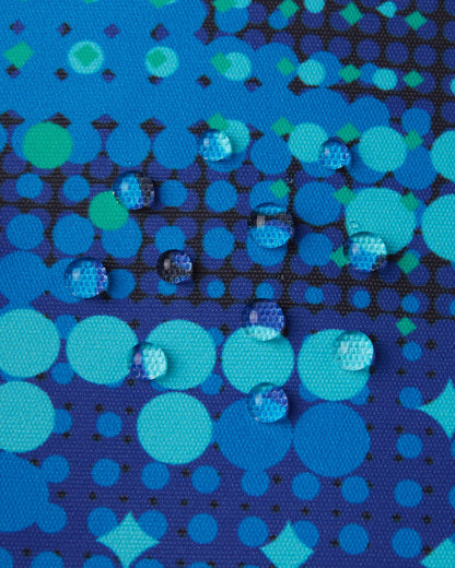Macro close-up of water droplets actively beading and rolling off the twilight blue patterned outer shell of the Reima Wingon kids' ski pants, visually highlighting the high-performance breathable and waterproof Reimatec technology.